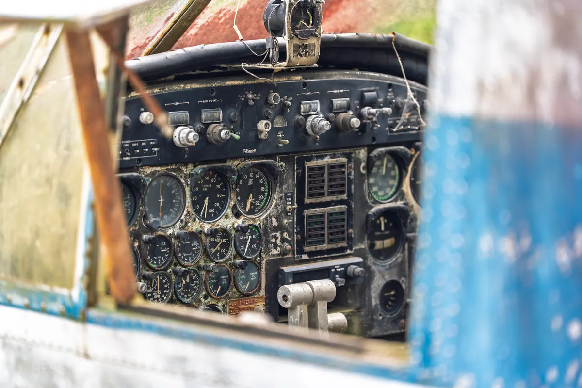 The weathered instrument panel and control yoke of an abandoned Twin Beech, seen through its broken cockpit window