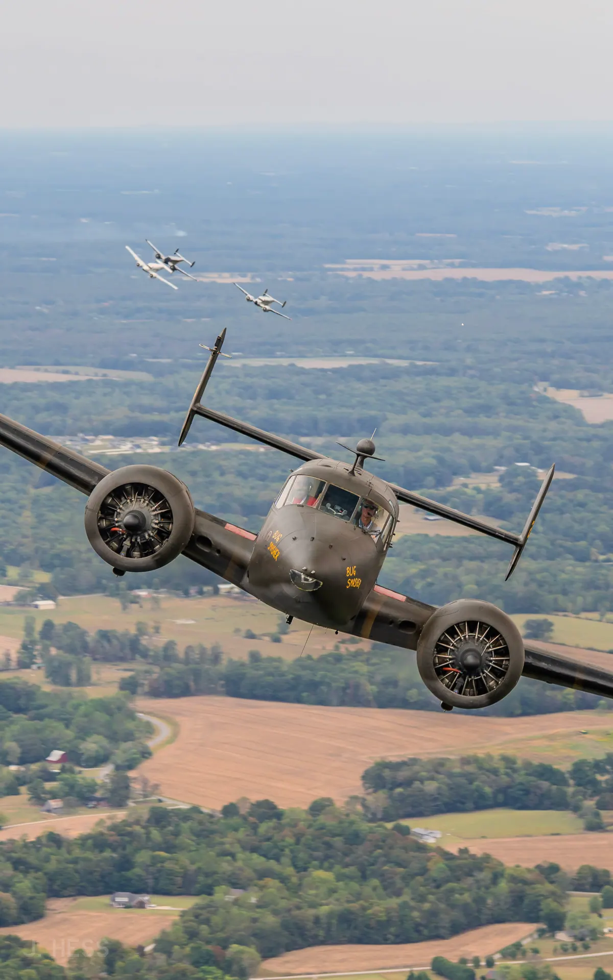 The olive-drab Beech 18 'Bug Smasher' banks toward the camera over Tennessee farmland, with three Twin Beeches following in the distance